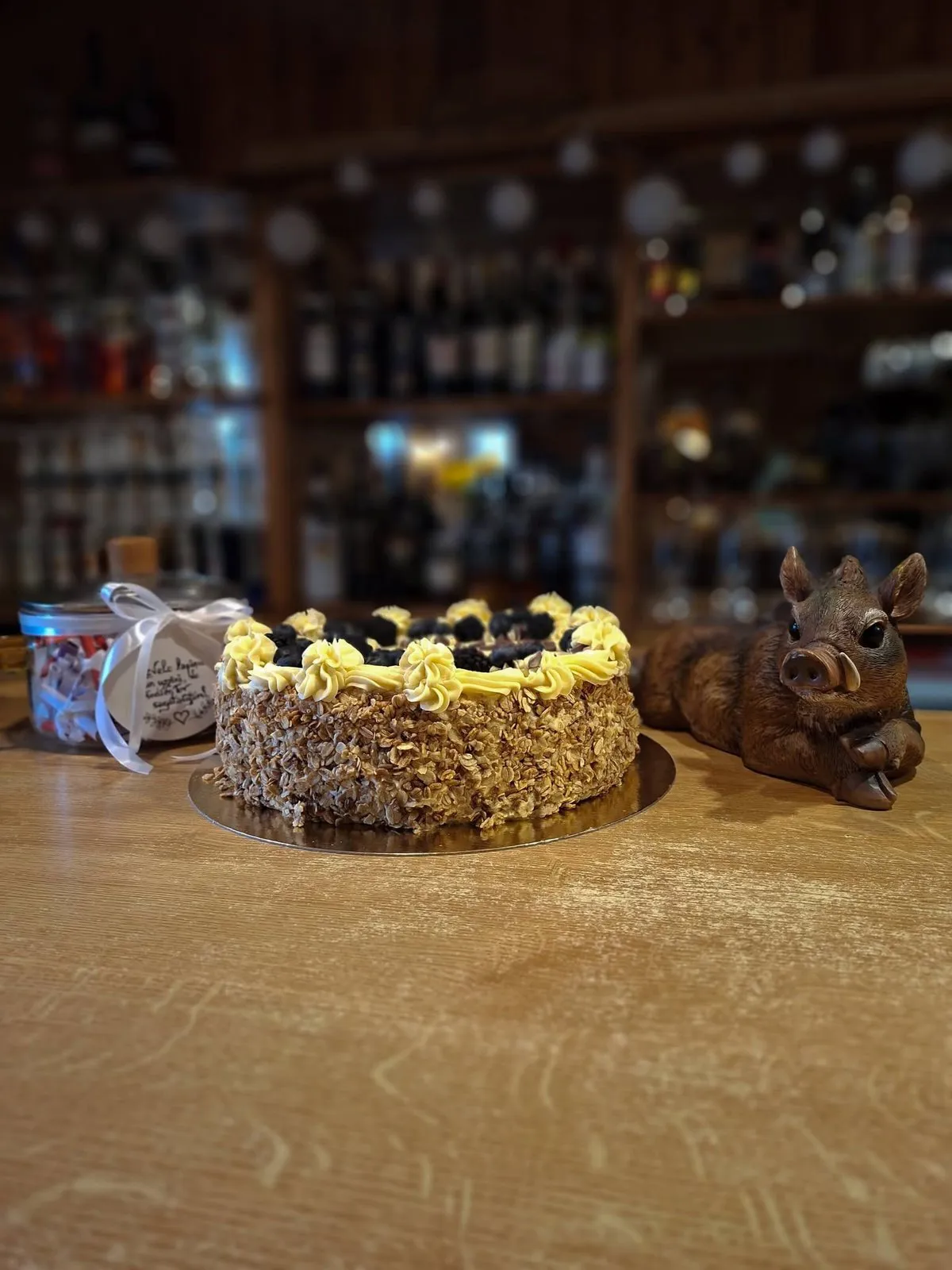 Torte ar ogām uz bāra letes, fonā plaukti ar pudelēm